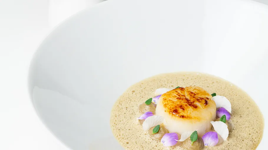 Seared scallop with decorative flowers in white dish.