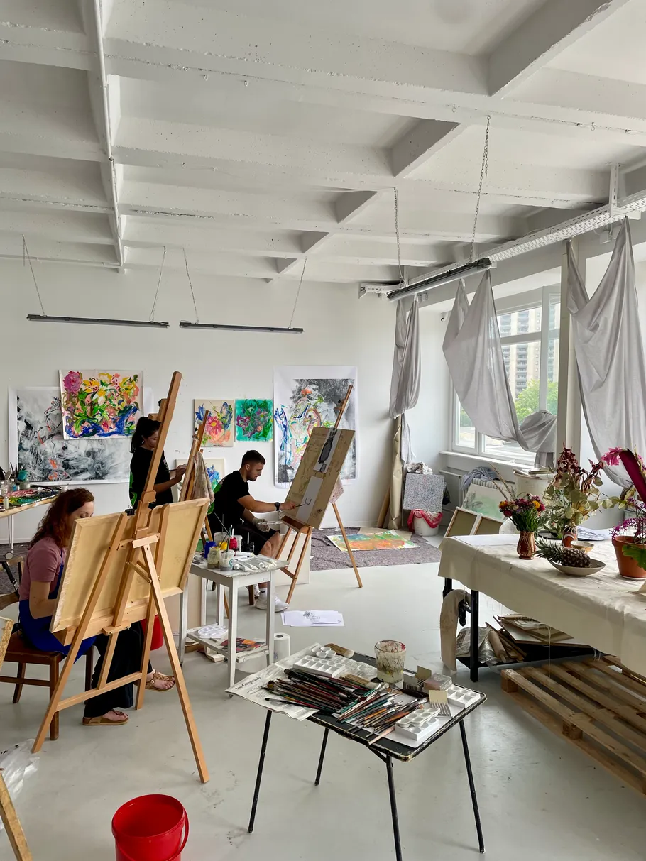 Artists painting on easels in bright studio.