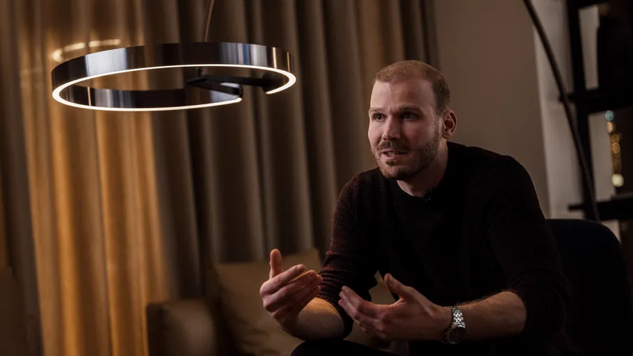 Man talking, gesturing, under modern lamp indoors.