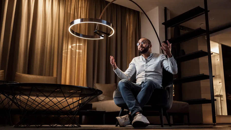 Mann sitzt unter moderner Lampe im Raum.