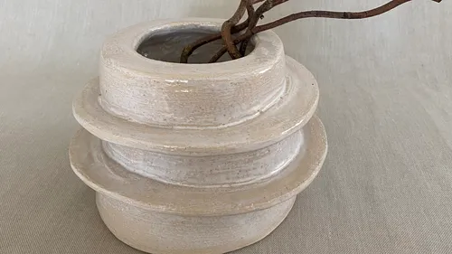 Weiße Keramikvase mit verdrehten Ästen darin.