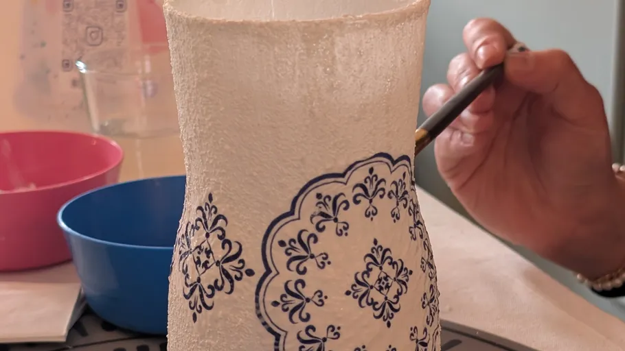 Person painting patterned vase in craft setting.