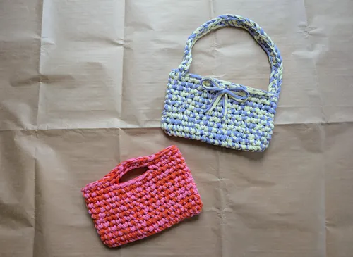 Zwei gehäkelte Taschen auf braunem Papierhintergrund.