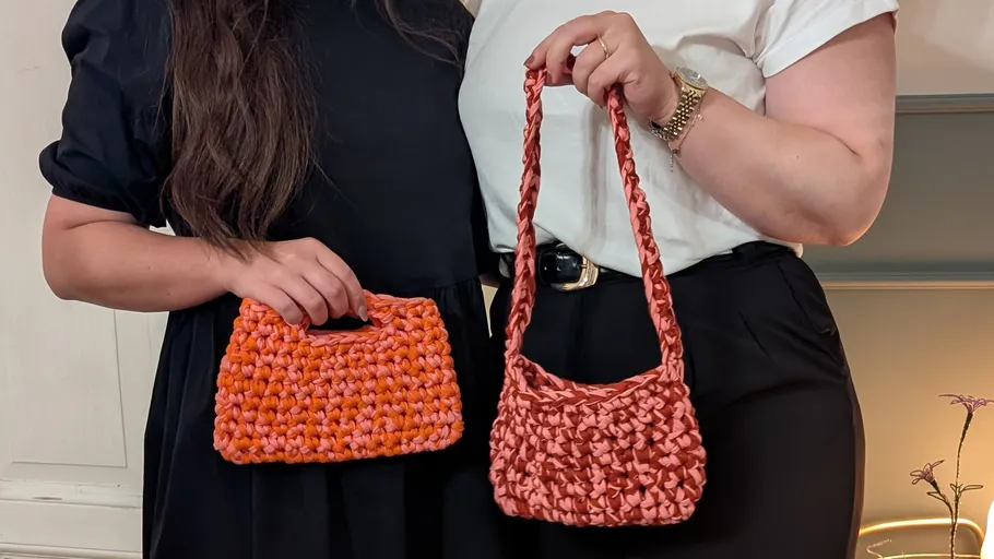 Two women holding handmade crochet handbags indoors.