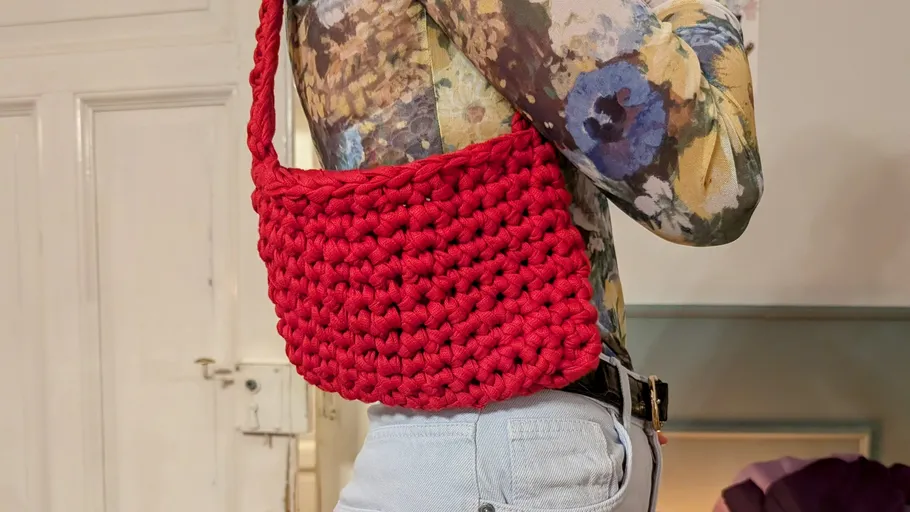 Red knitted bag carried by person indoors.