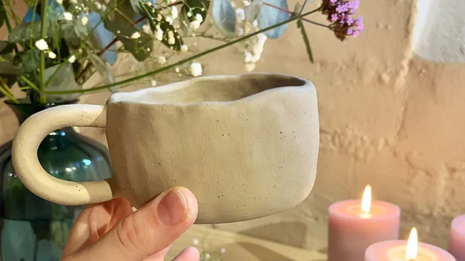 Hand hält rustikalen Becher, Blumenvase, brennende Kerzen.