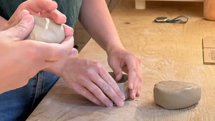 Hände formen Ton auf Holztisch.