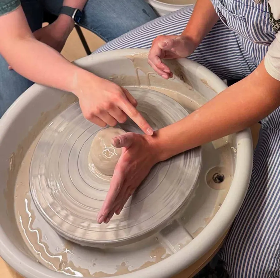Hands shaping clay on pottery wheel.
