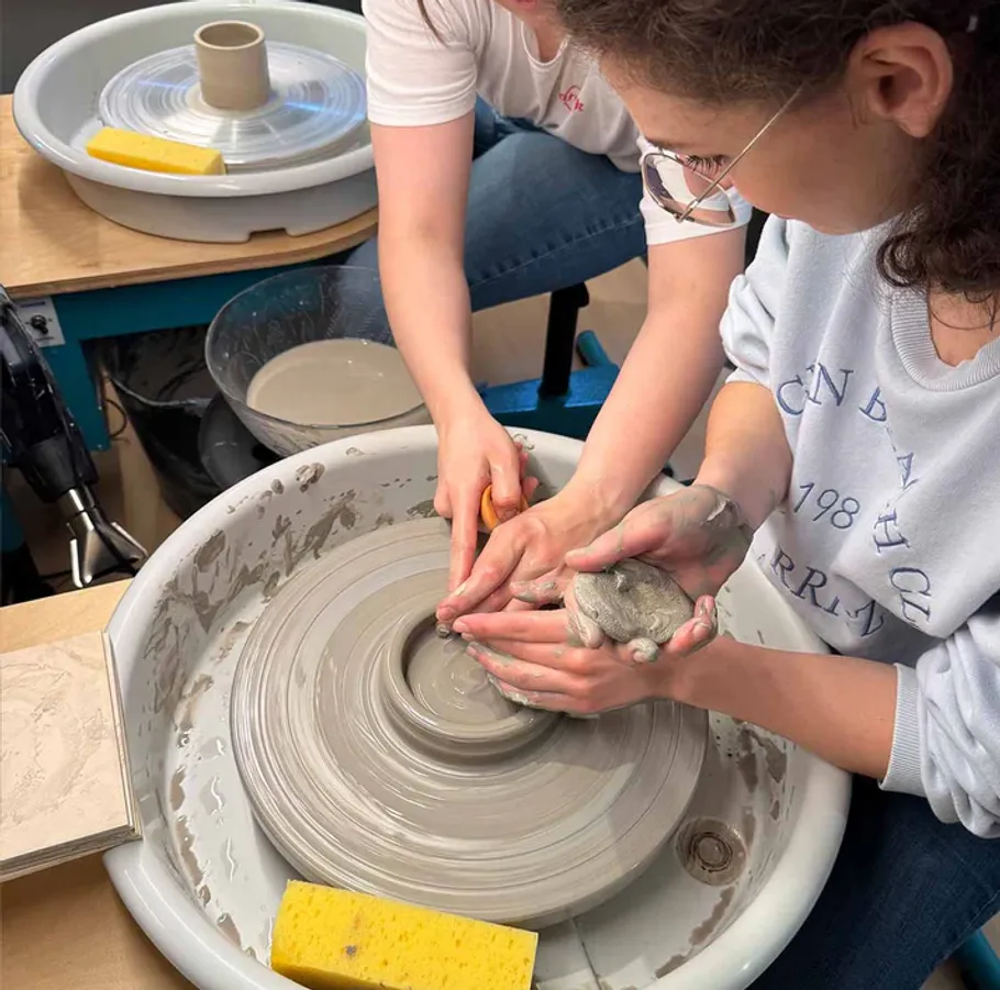 Two people shaping clay on pottery wheel.