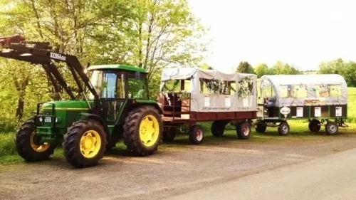 Grüner Traktor zieht zwei überdachte Anhänger im Freien.