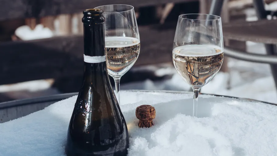 Champagnerflasche und Gläser auf Schneeoberfläche.