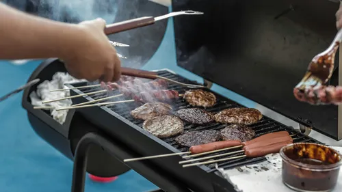 Hände grillen Fleisch und Würstchen im Freien.