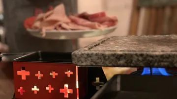 Raclette-Grill mit verschiedenen Fleischsorten in der Nähe.