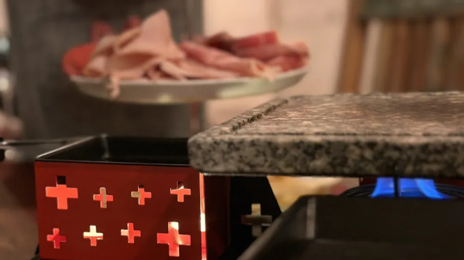 Raclette-Grill mit verschiedenen Fleischsorten in der Nähe.