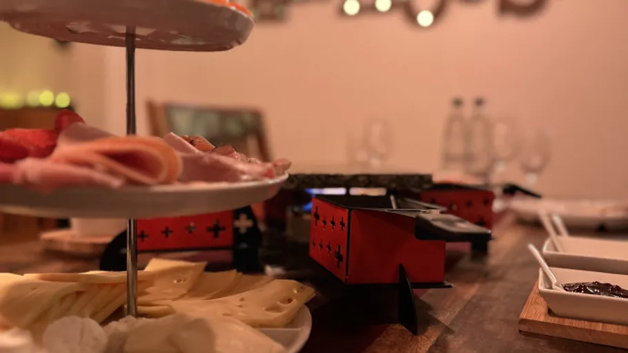 Raclette-Tisch mit Fleisch und Käse gedeckt.