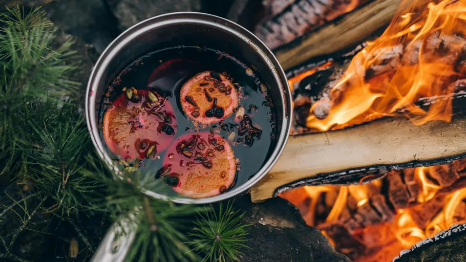 Pot of mulled wine beside a campfire.