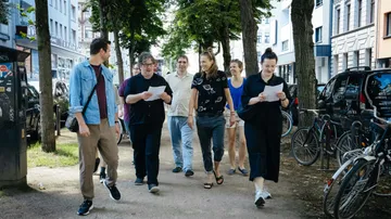 Gruppe von Menschen geht auf baumgesäumter Straße.