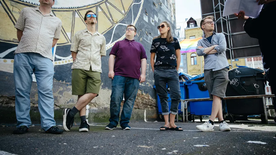 Five people standing with urban mural background.