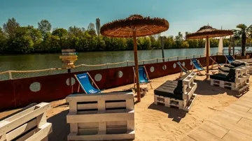 Sandstrand mit Liegestühlen neben Fluss.