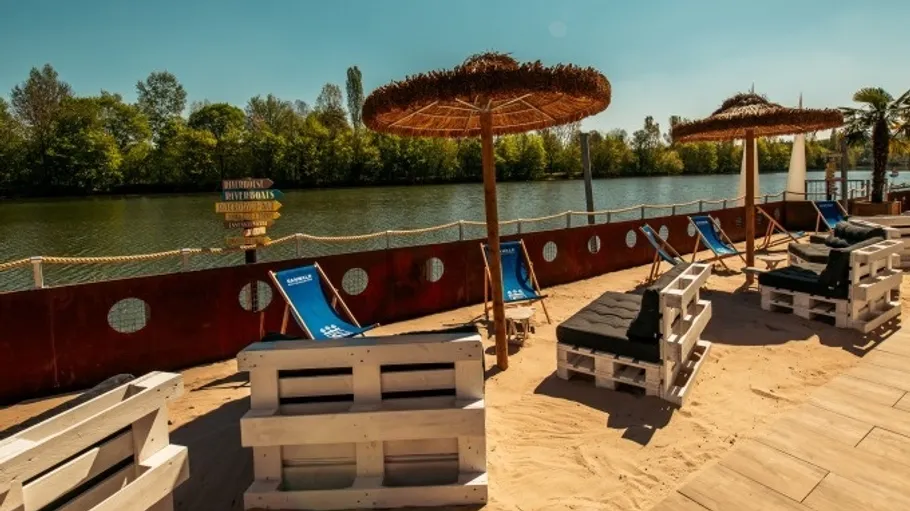 Sandstrand mit Liegestühlen neben Fluss.