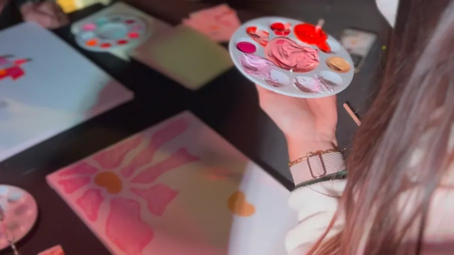 Person holding paint palette near painted canvas.