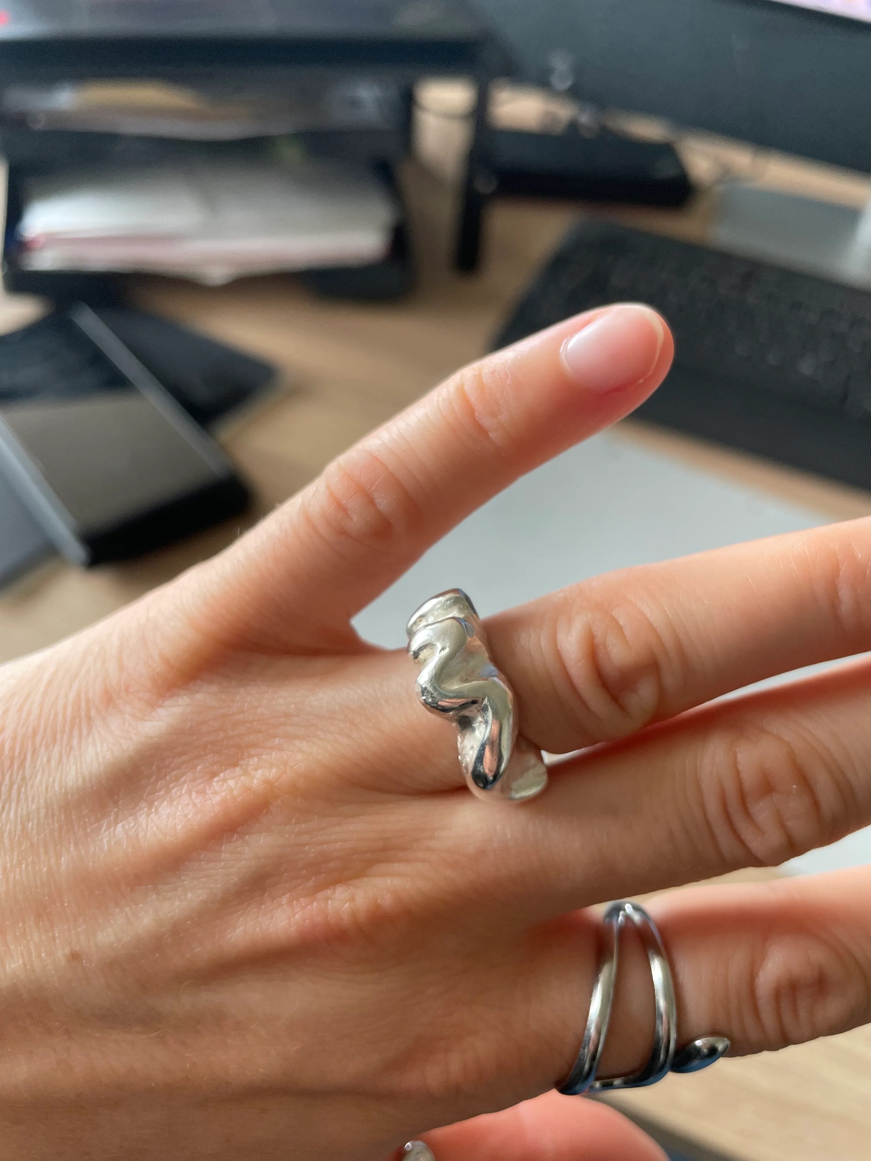 Hand trägt silberne Ringe vor Schreibtischhintergrund.