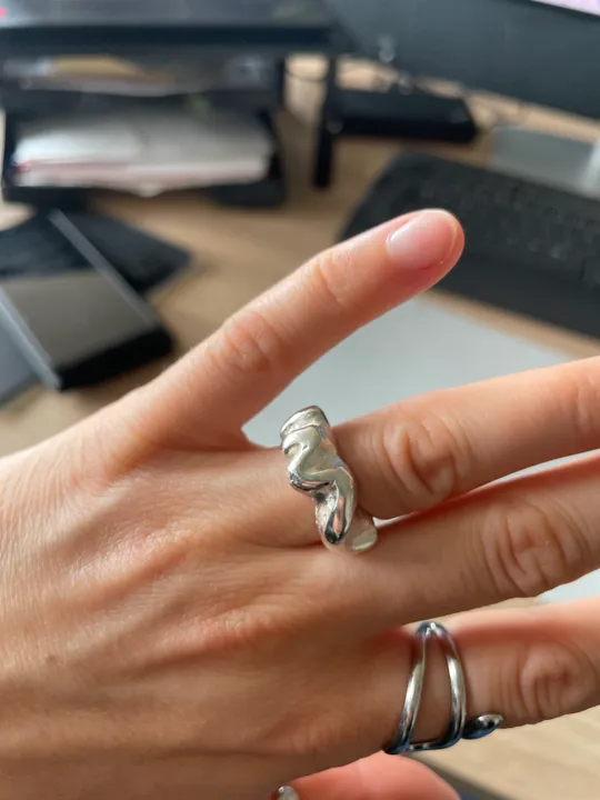 Hand trägt silberne Ringe vor Schreibtischhintergrund.