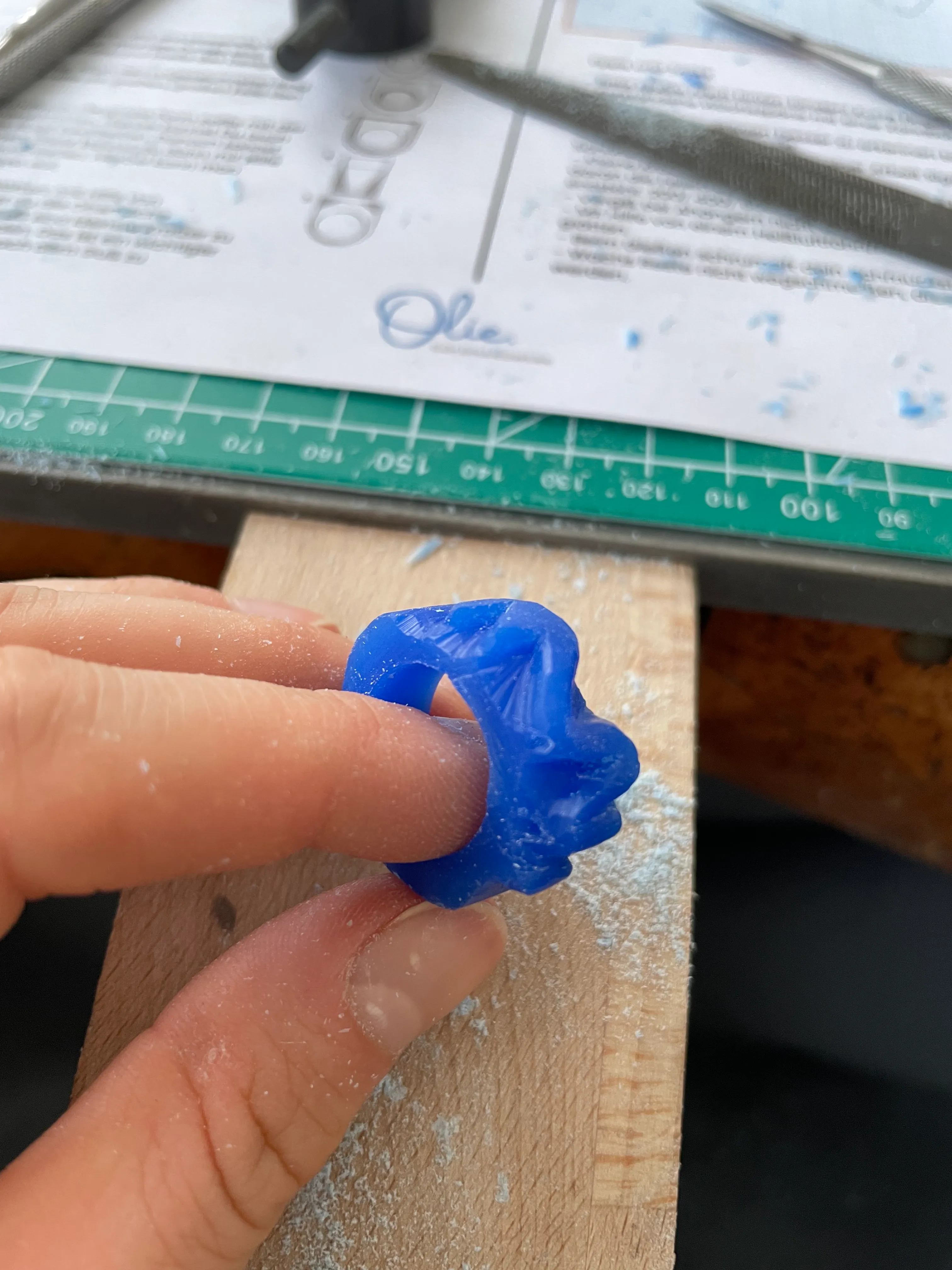 Hand hält einen blauen geschnitzten Wachsrings.