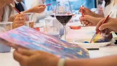 People painting with wine glasses on table.