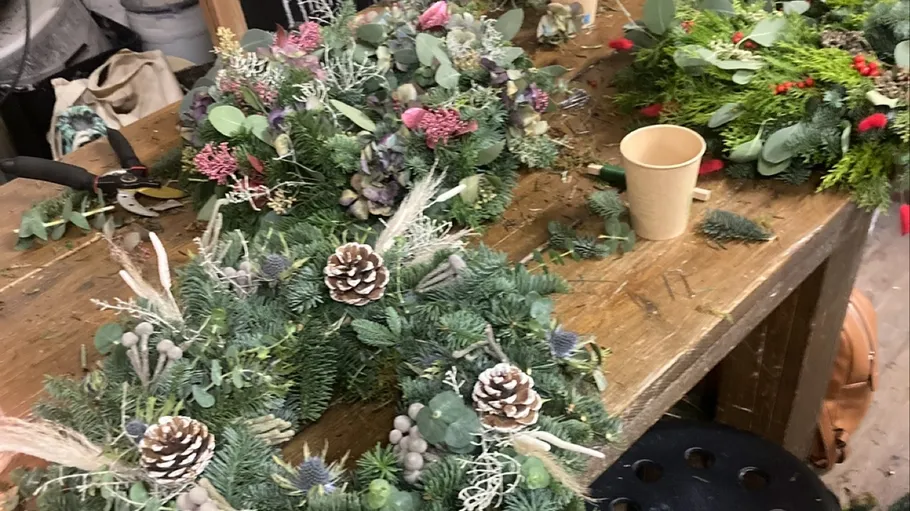Floral wreaths being crafted on wooden table.
