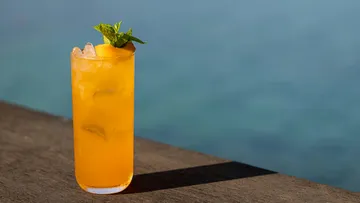 Oranger Cocktail mit Minze am Wasser.