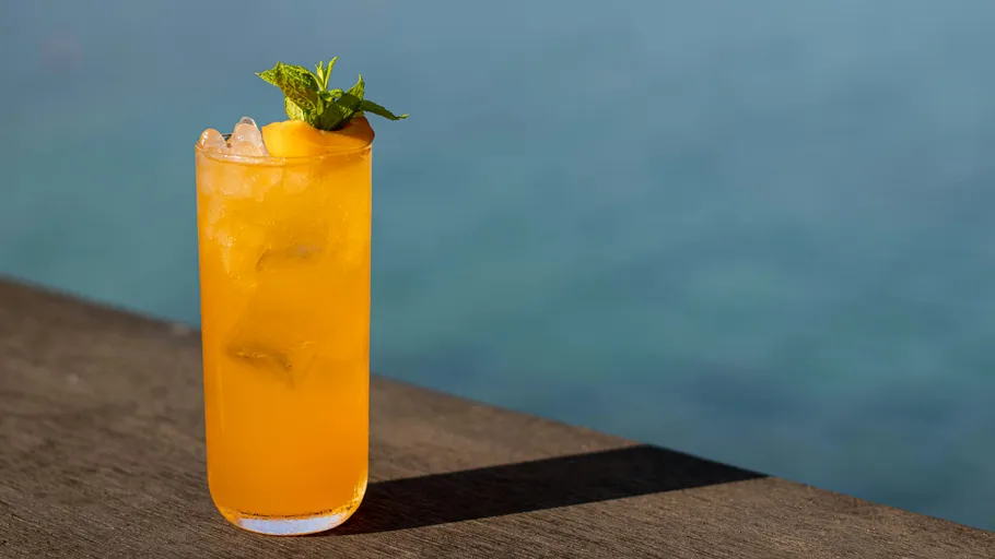 Oranger Cocktail mit Minze am Wasser.