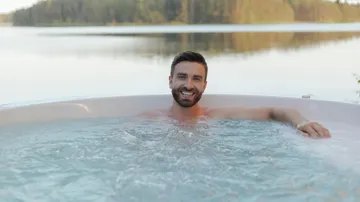 Man relaxing in outdoor hot tub by lake.