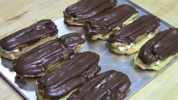 Chocolate eclairs on a metal tray.