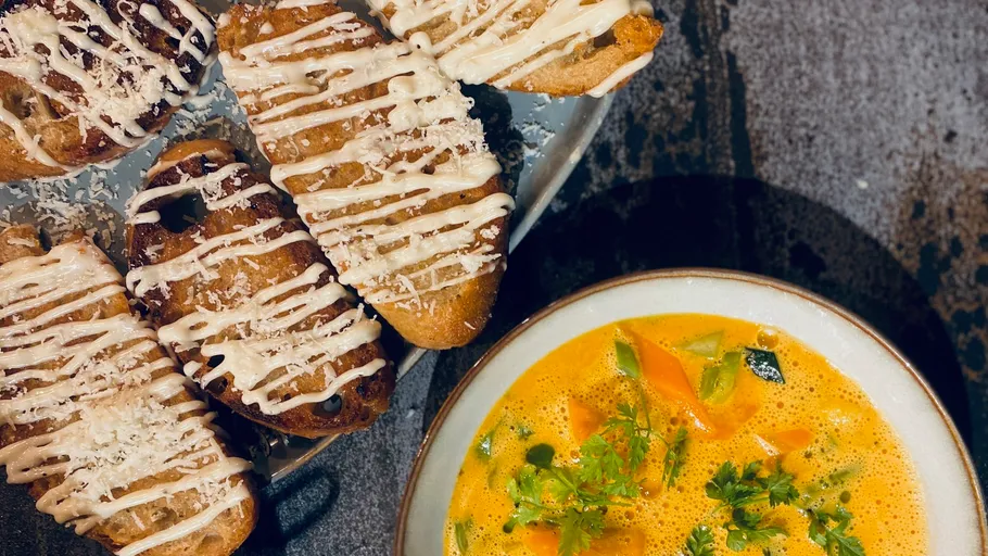Teller mit bestrichenem Brot neben Gemüsesuppe.