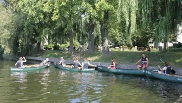 People paddling in canoes near a tree-lined shore.