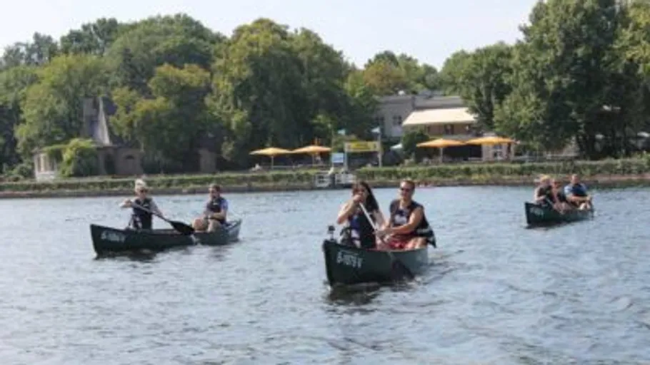 Menschen paddeln Kanus auf einem See, Bäume im Hintergrund.
