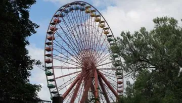 Riesenrad überragt Bäume, bewölkter Himmel.