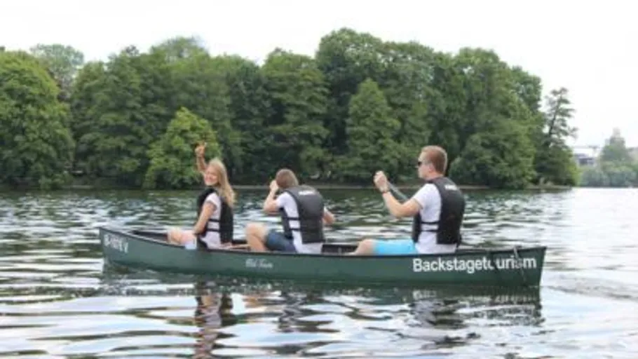 Drei Personen paddeln ein Kanu auf einem See.