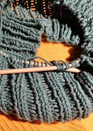 Strickprojekt mit blauem Garn auf Nadeln.