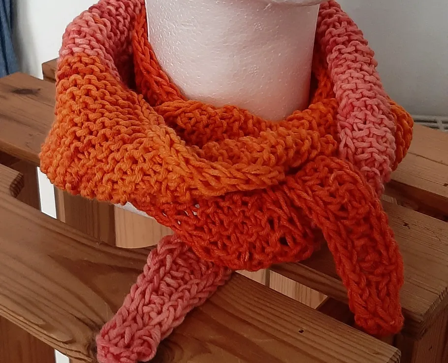 Knitted orange scarf on wooden rack.