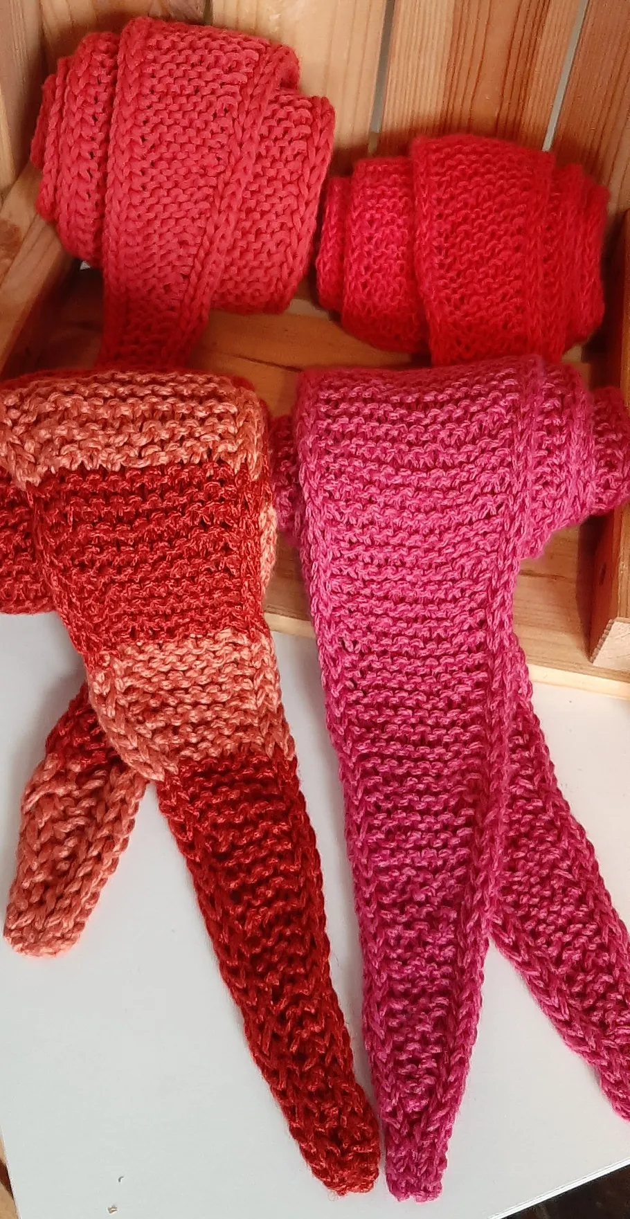 Knitted scarves rolled and draped, wooden box.