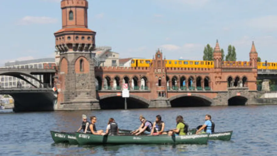 Menschen paddeln im Kanu nahe einer historischen Brücke.