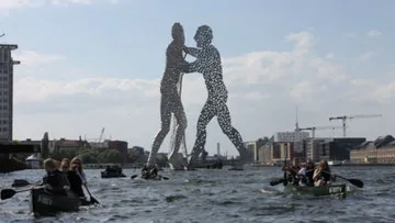 Kanus auf Fluss nahe großer Skulptur.