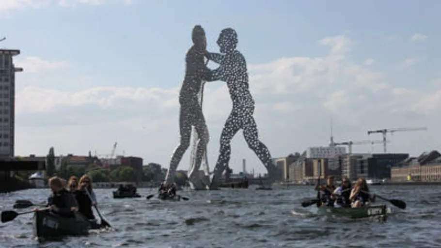 Kanus auf Fluss nahe großer Skulptur.