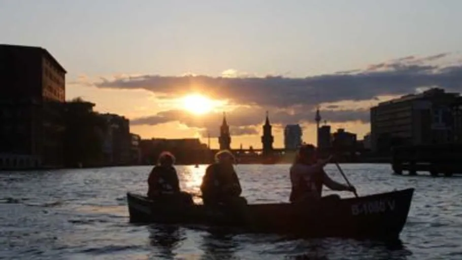 Personen paddeln auf Fluss bei Sonnenuntergang.