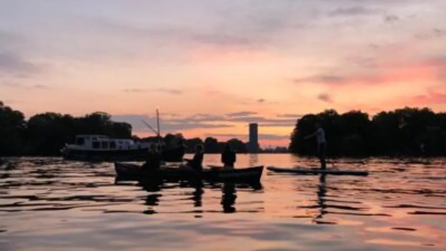 Menschen beim Kanufahren und Paddleboarden bei Sonnenuntergang.