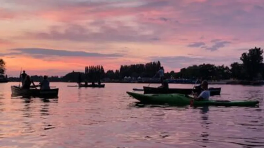 Menschen beim Kajakfahren auf See bei Sonnenuntergang.