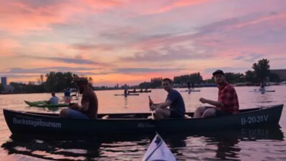 Three people canoeing on a lake at sunset.