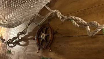 Ship wheel on wooden wall with rope decor.